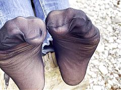 Feet in black and grey nylon socks wiggling toes at the seashore
